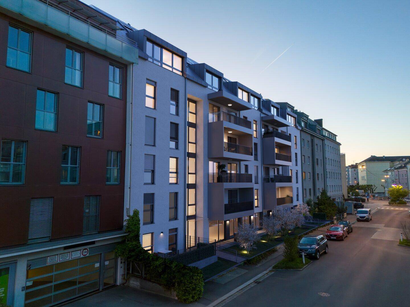 Moderne Wohngebäude an einer Straße in der Dämmerung mit beleuchteten Fenstern.