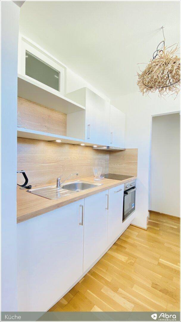 Kompakte Küche mit weißen Schränken, Holz-Arbeitsplatte und integriertem Backofen.