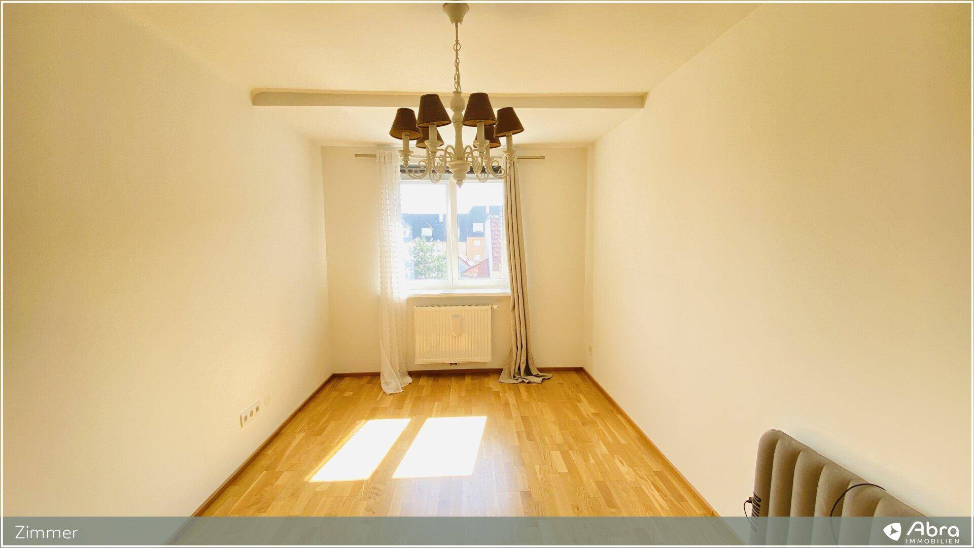 Geräumiges Zimmer mit Holzboden, einem Fenster und einem eleganten Kronleuchter.