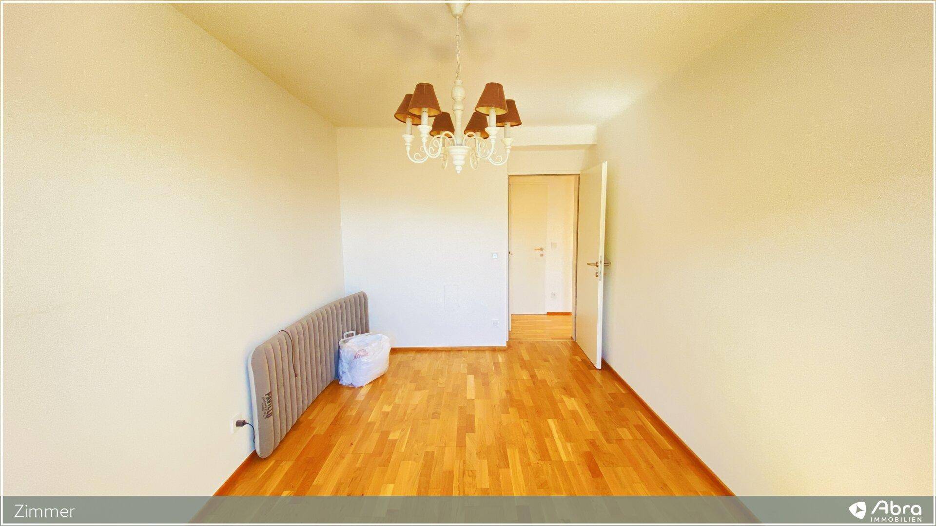 Leeres Zimmer mit Holzboden und einem klassischen Kronleuchter, bereit zur Einrichtung.