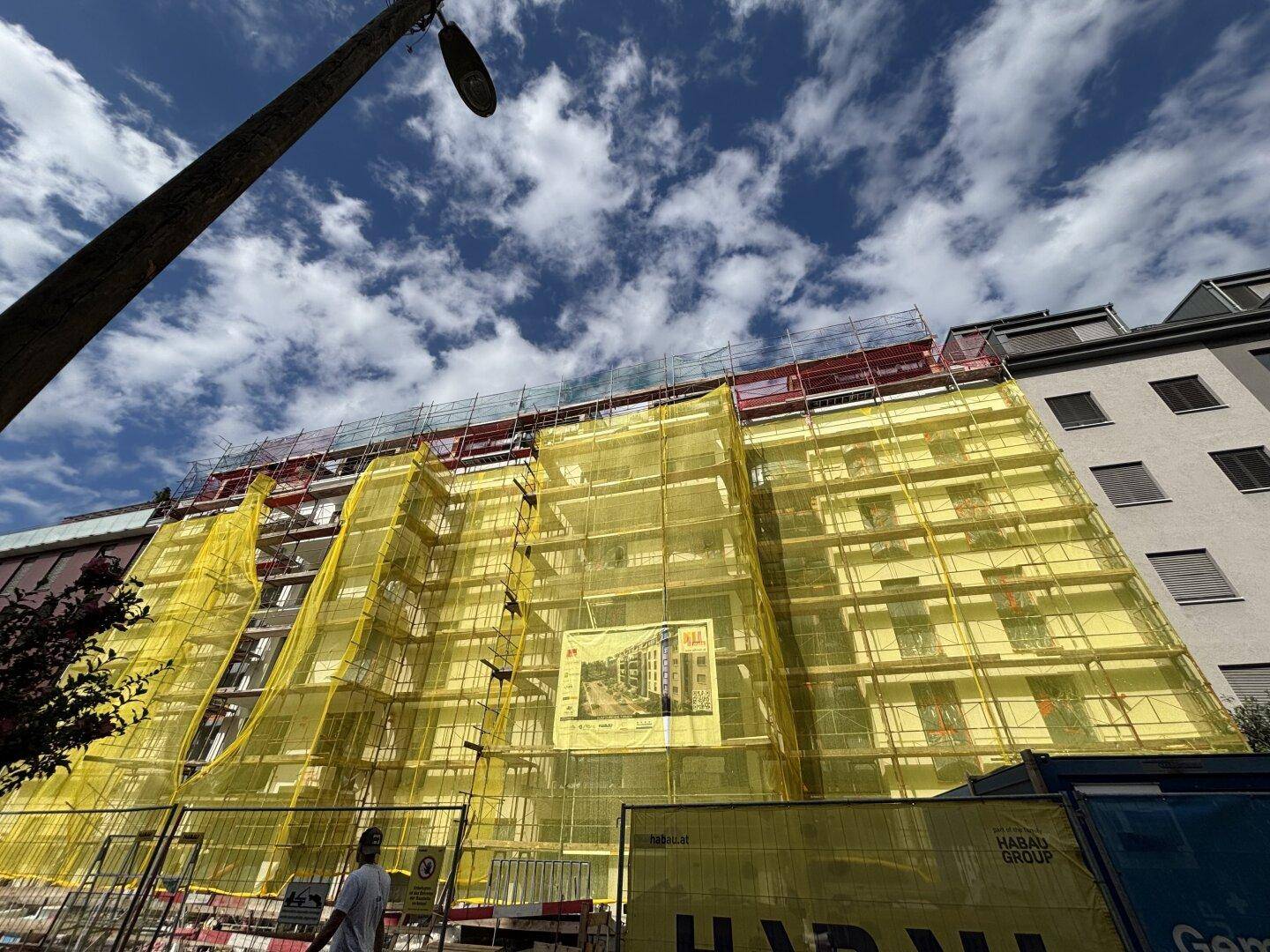 Gebäude unter Renovierung mit Gerüst und gelbem Schutznetz unter blauem Himmel.