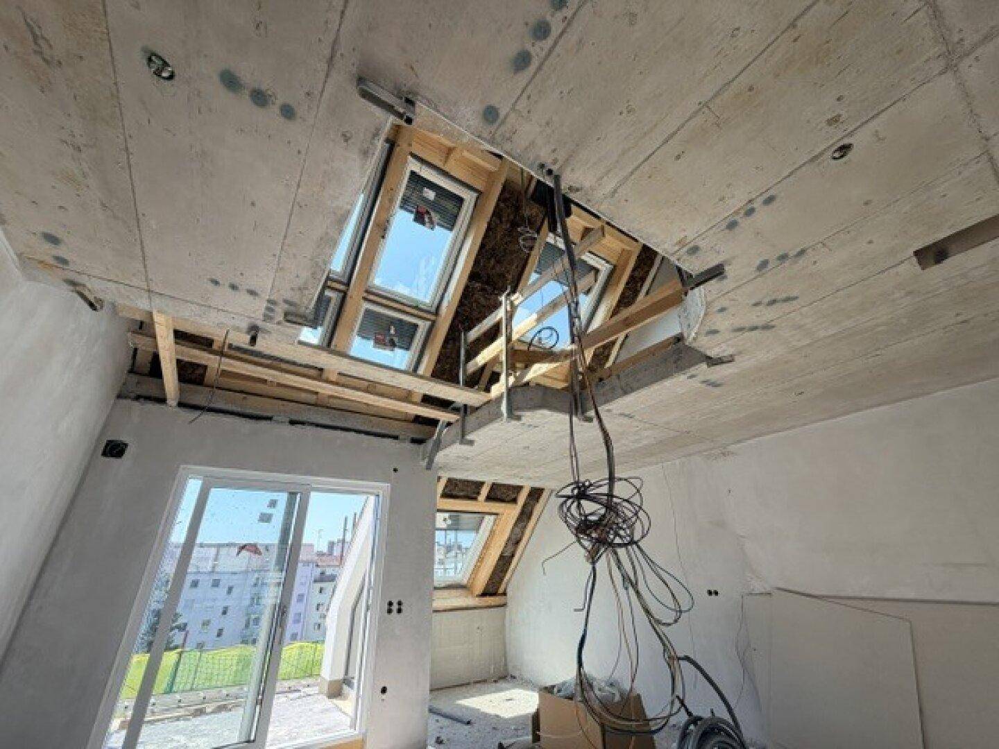 Rohbau eines Dachgeschosses mit großen Schiebefenstern und sichtbaren Deckenstrukturen, viel Tageslicht.