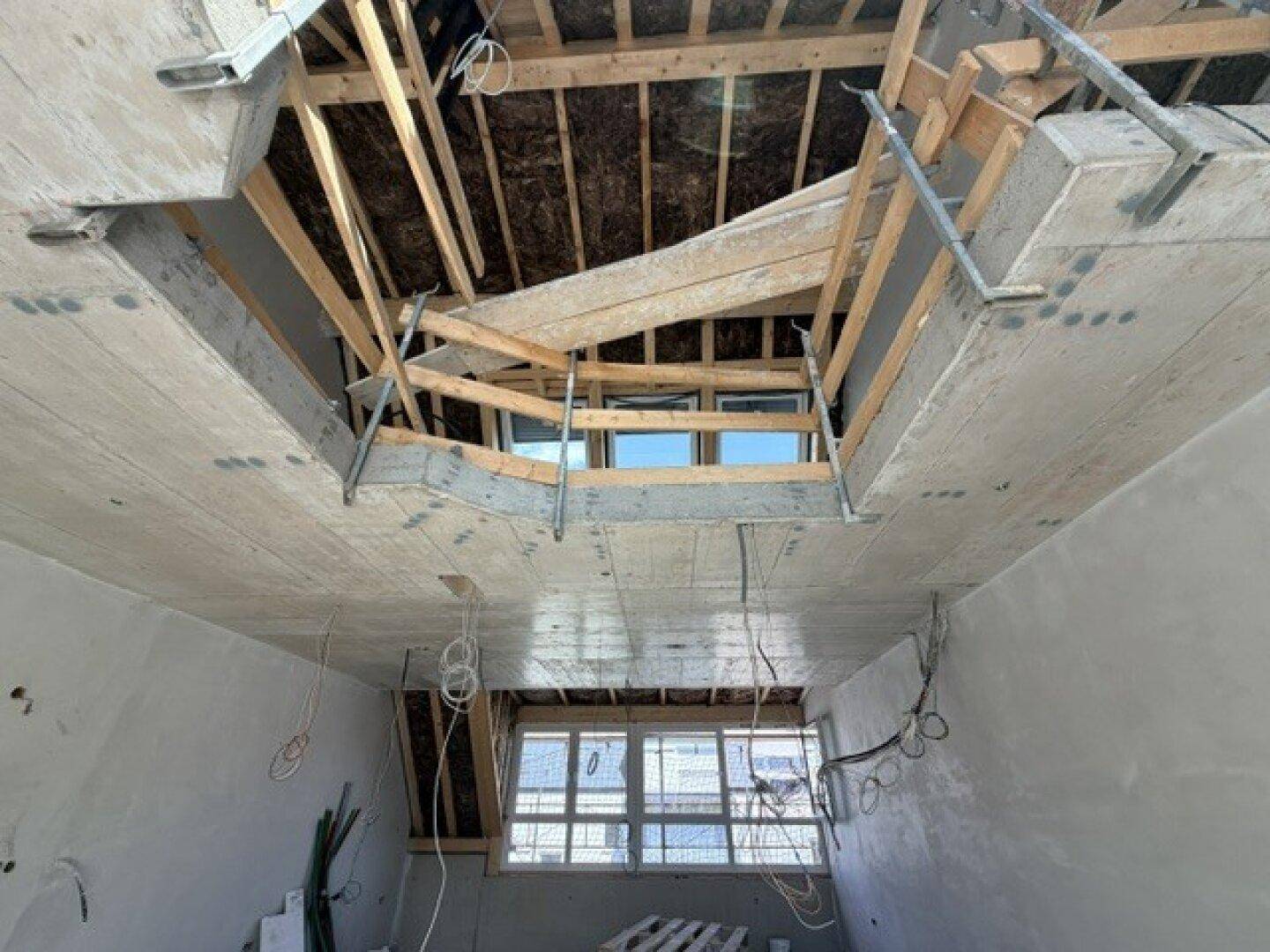 Blick auf die Deckenkonstruktion im Rohbau mit sichtbaren Holzbalken und mehreren Dachfenstern.