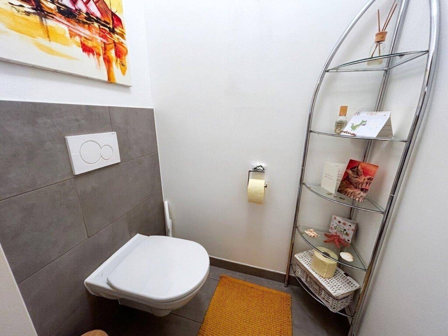 Modernes Gäste-WC mit wandhängender Toilette und dekorativem Regal.