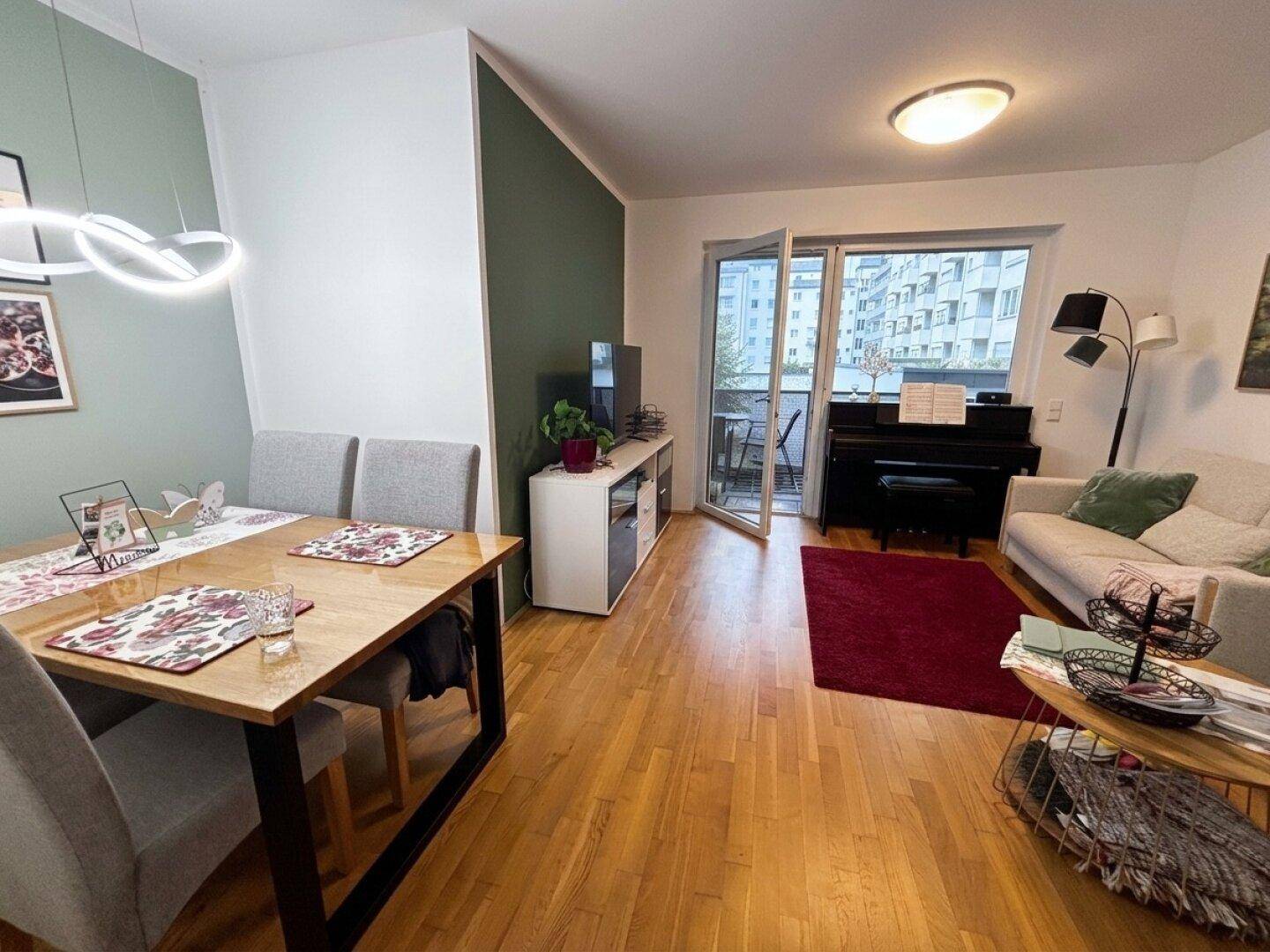Heller Wohn-Essbereich mit Holzboden, Esstisch und Zugang zum Balkon.