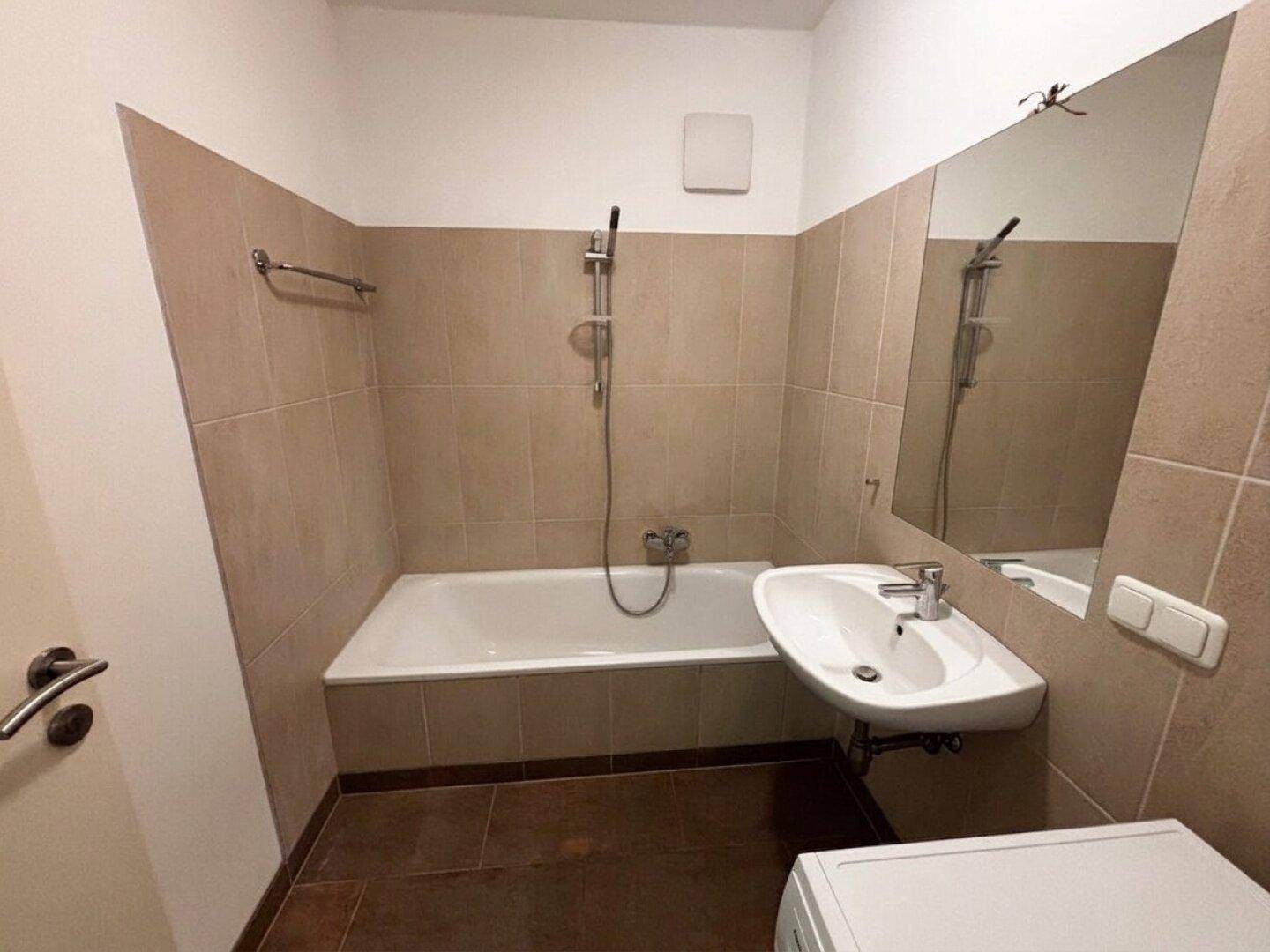 Funktionales Badezimmer mit Badewanne, Waschbecken und beigefarbenen Fliesen, gut gepflegt.