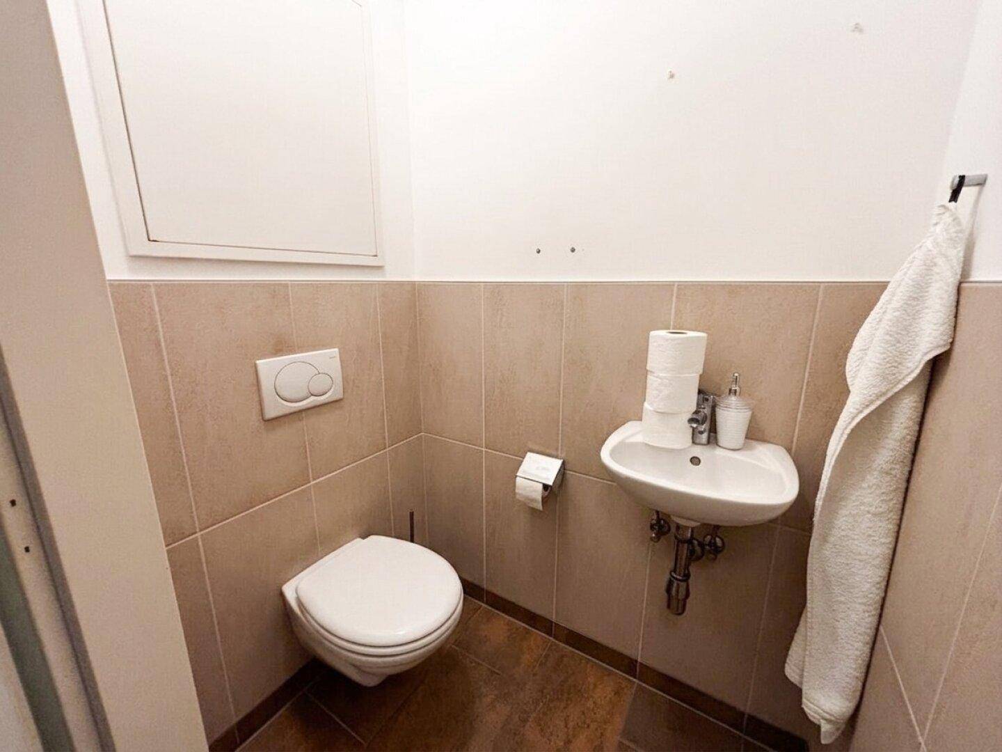 Kleines Gäste-WC mit wandhängender Toilette und Handwaschbecken, in neutralen Farbtönen.