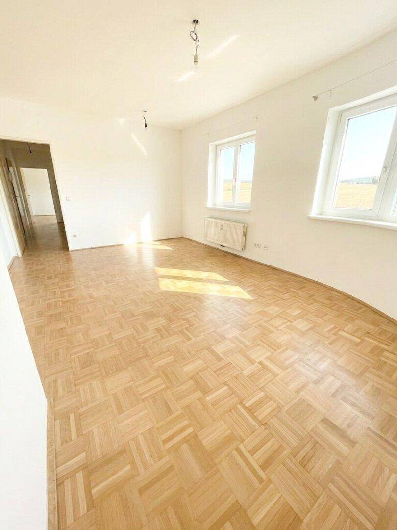Geräumiges Zimmer mit Parkettboden und zwei Fenstern, die den Raum hell erscheinen lassen.