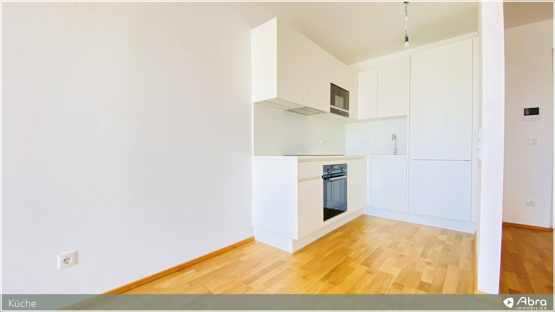Helle Einbauküche mit weißen Fronten, integriertem Backofen und Holzparkettboden.