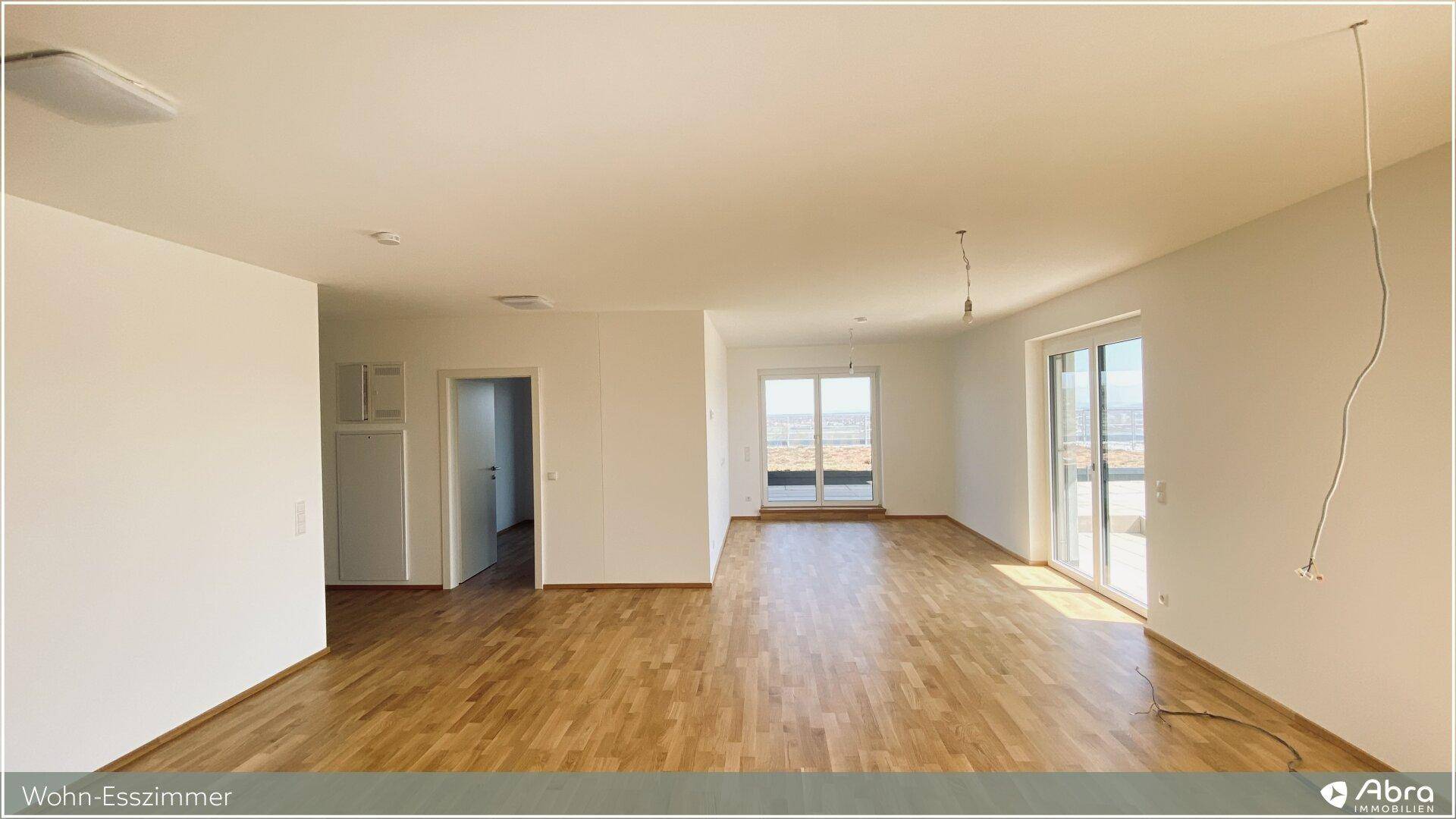 Geräumiger, heller Wohn-Essbereich mit Parkettboden und Zugang zu einer Terrasse oder Balkon.