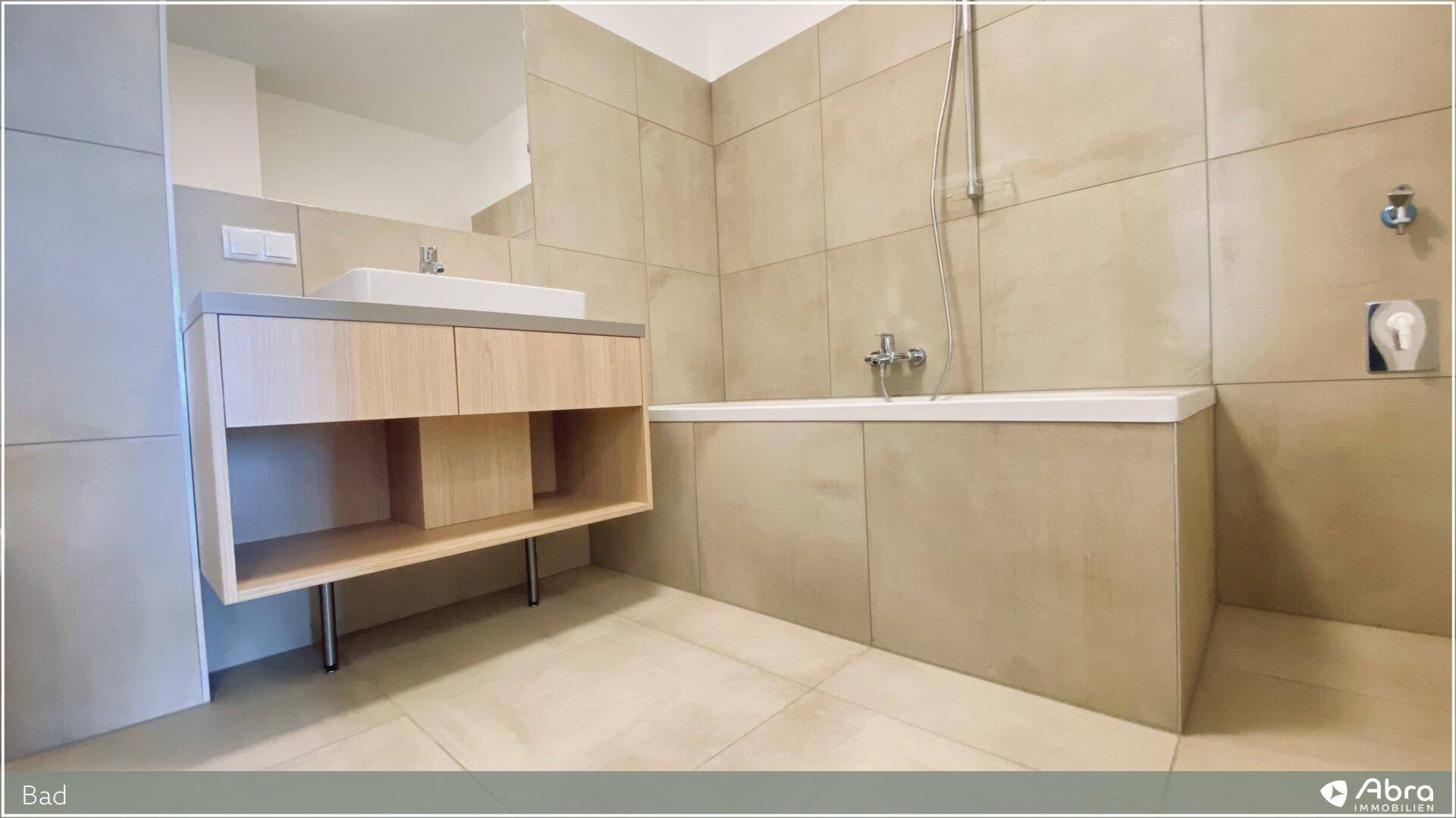 Modernes Badezimmer mit beigefarbenen Fliesen, Badewanne und stilvollem Waschtischunterschrank.