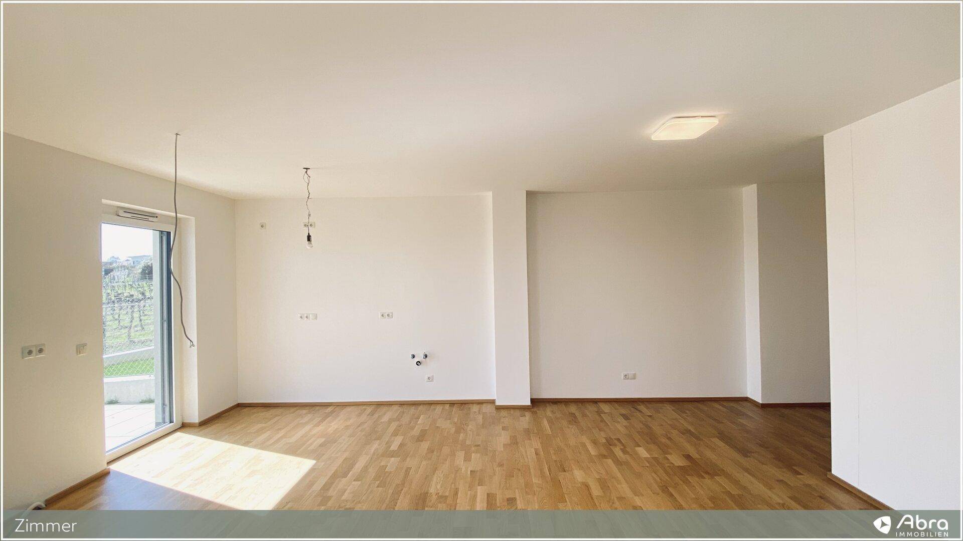 Geräumiger Raum mit Parkettboden und großem Fenster, das den Zugang nach draußen ermöglicht.