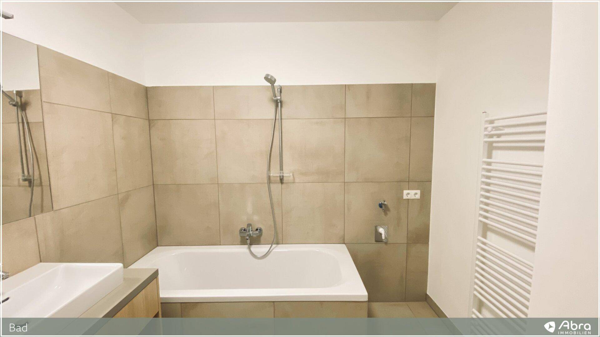 Badezimmer mit Badewanne und praktischem beheiztem Handtuchhalter, in neutralen Farbtönen.
