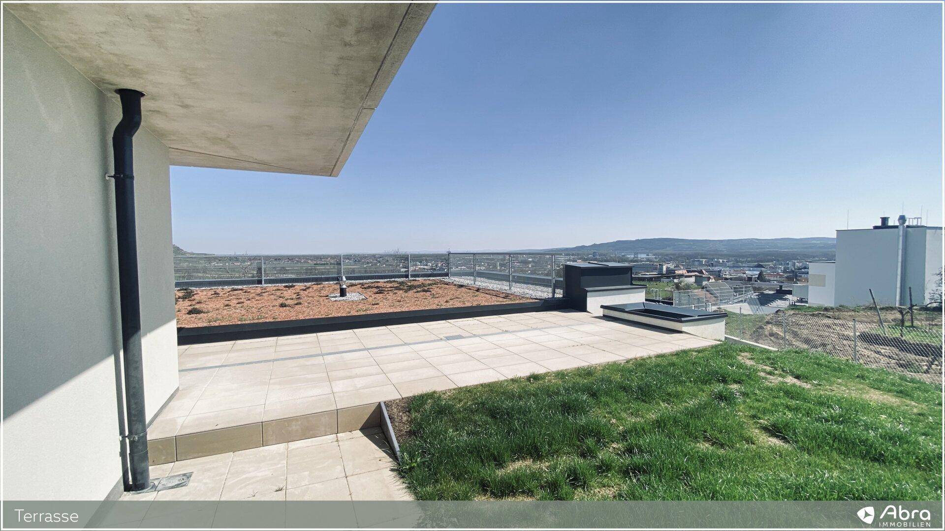 Weitläufige Dachterrasse mit Fliesen und Grünfläche, bietet einen Panoramablick über die Landschaft.