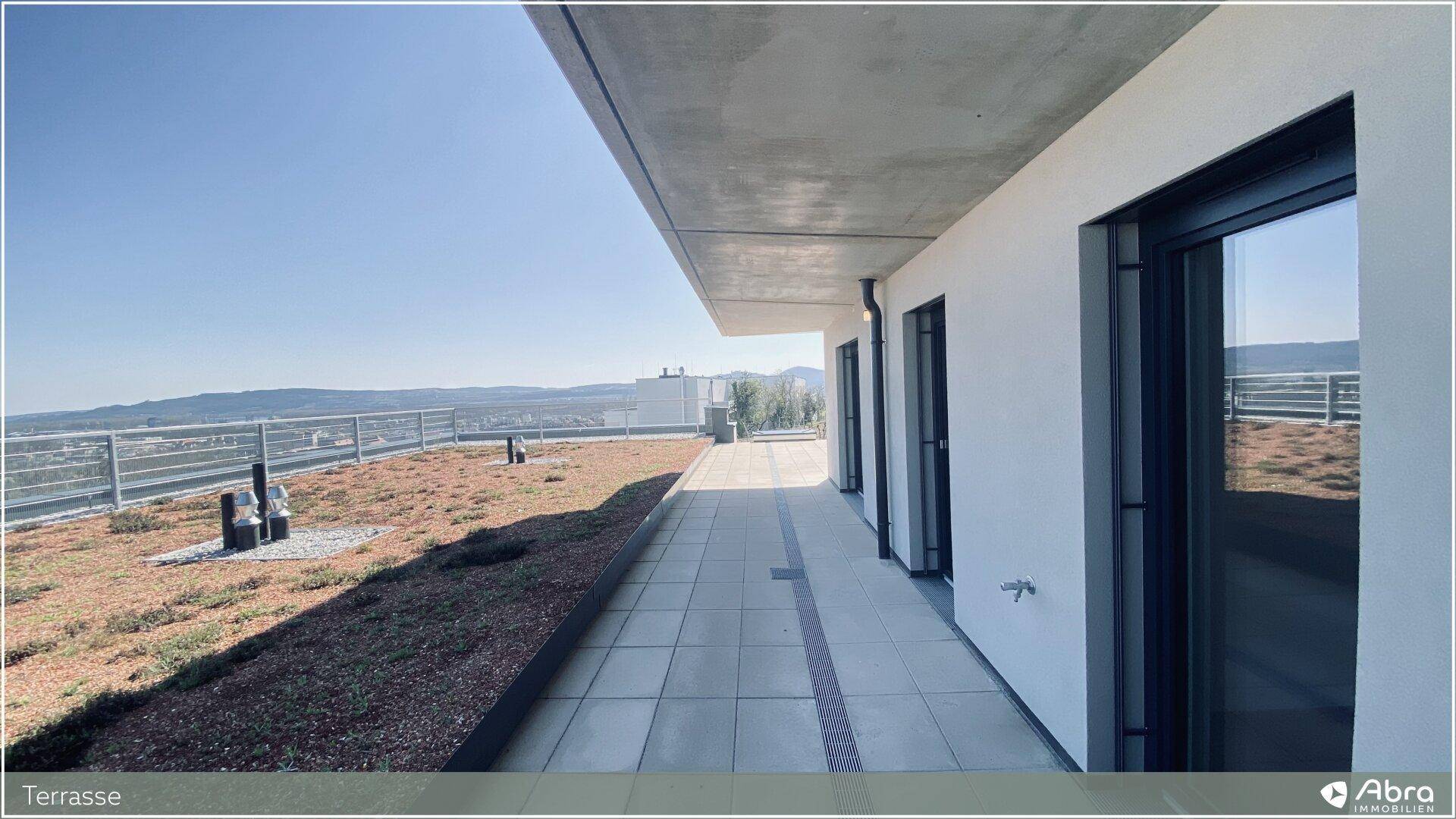 Große Dachterrasse mit Fliesenboden, Gründach und weitem Blick über die Landschaft und Stadt.