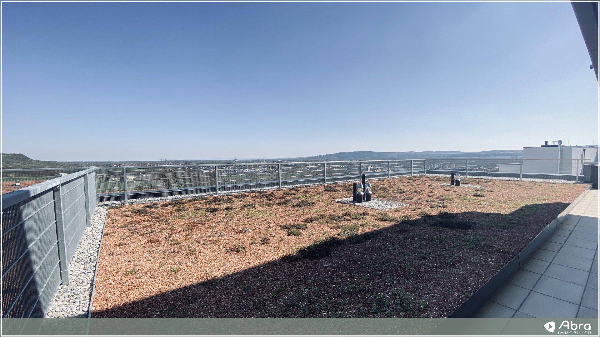 Weitläufige Dachterrasse mit Kiesfläche und Panoramablick über die umliegende Landschaft und Stadt.