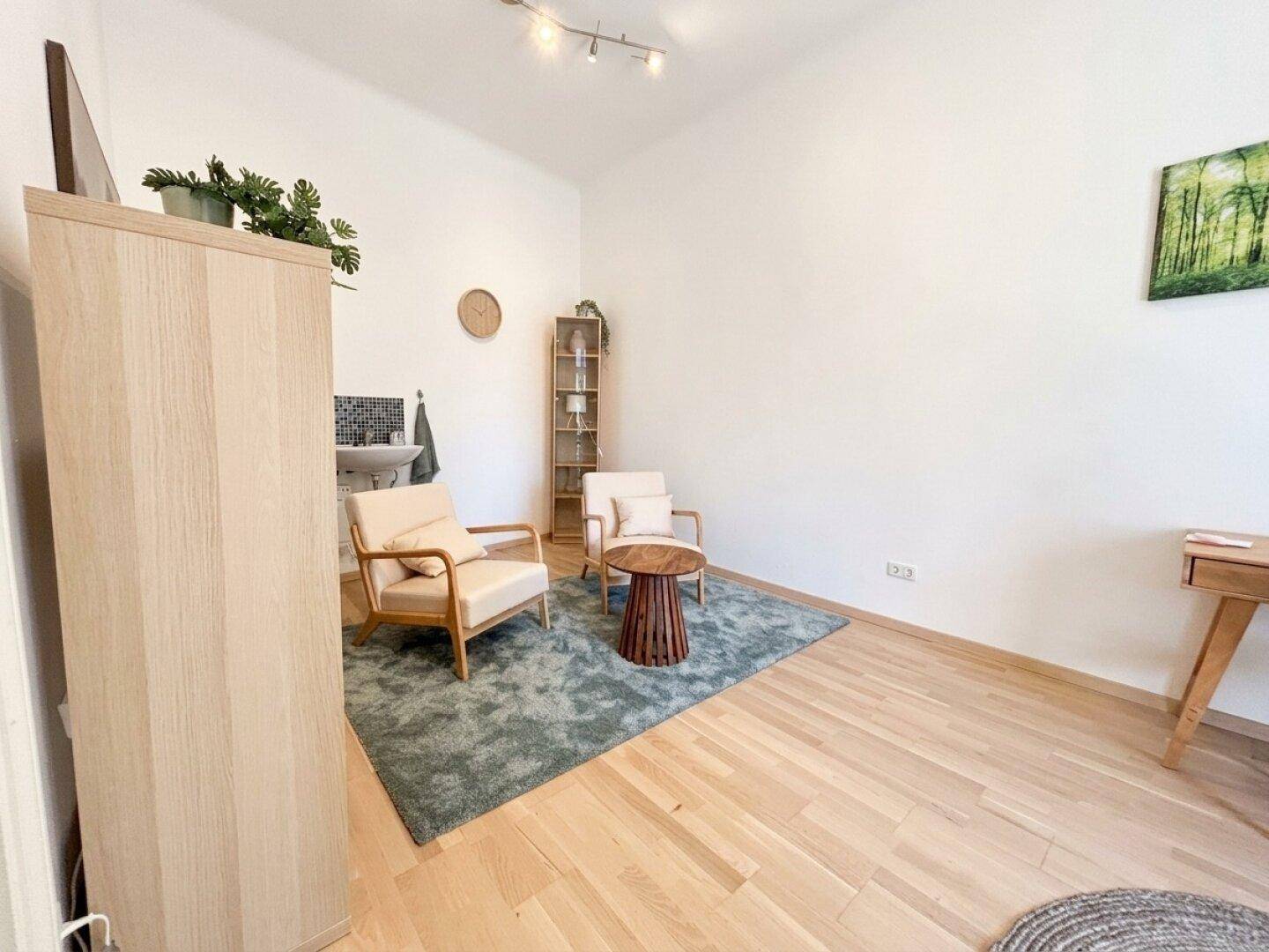 Heller Büroraum mit Holzboden, Sitzgelegenheiten und einem hohen Holzschrank, der Stauraum bietet.
