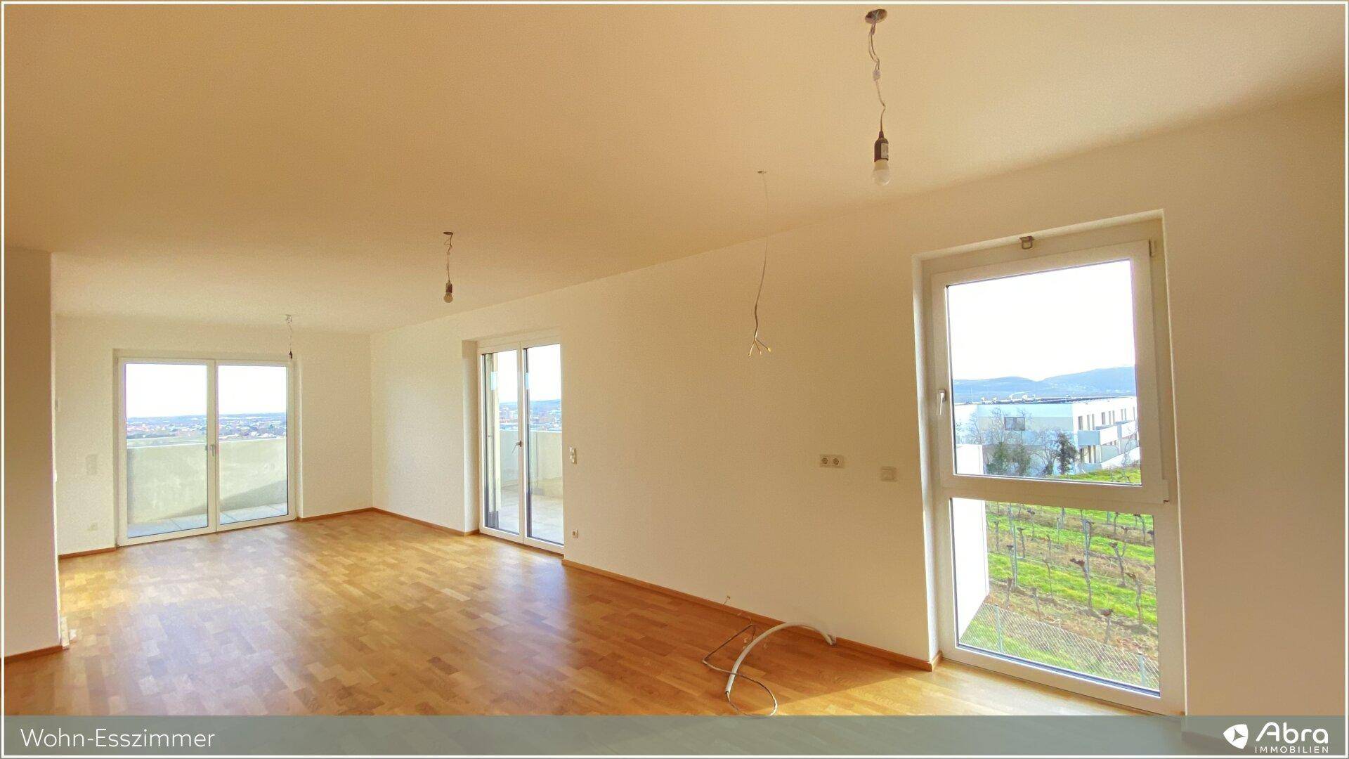 Heller Wohn-Essbereich mit Parkettboden, großen Fenstern und Zugang zu einem Balkon.