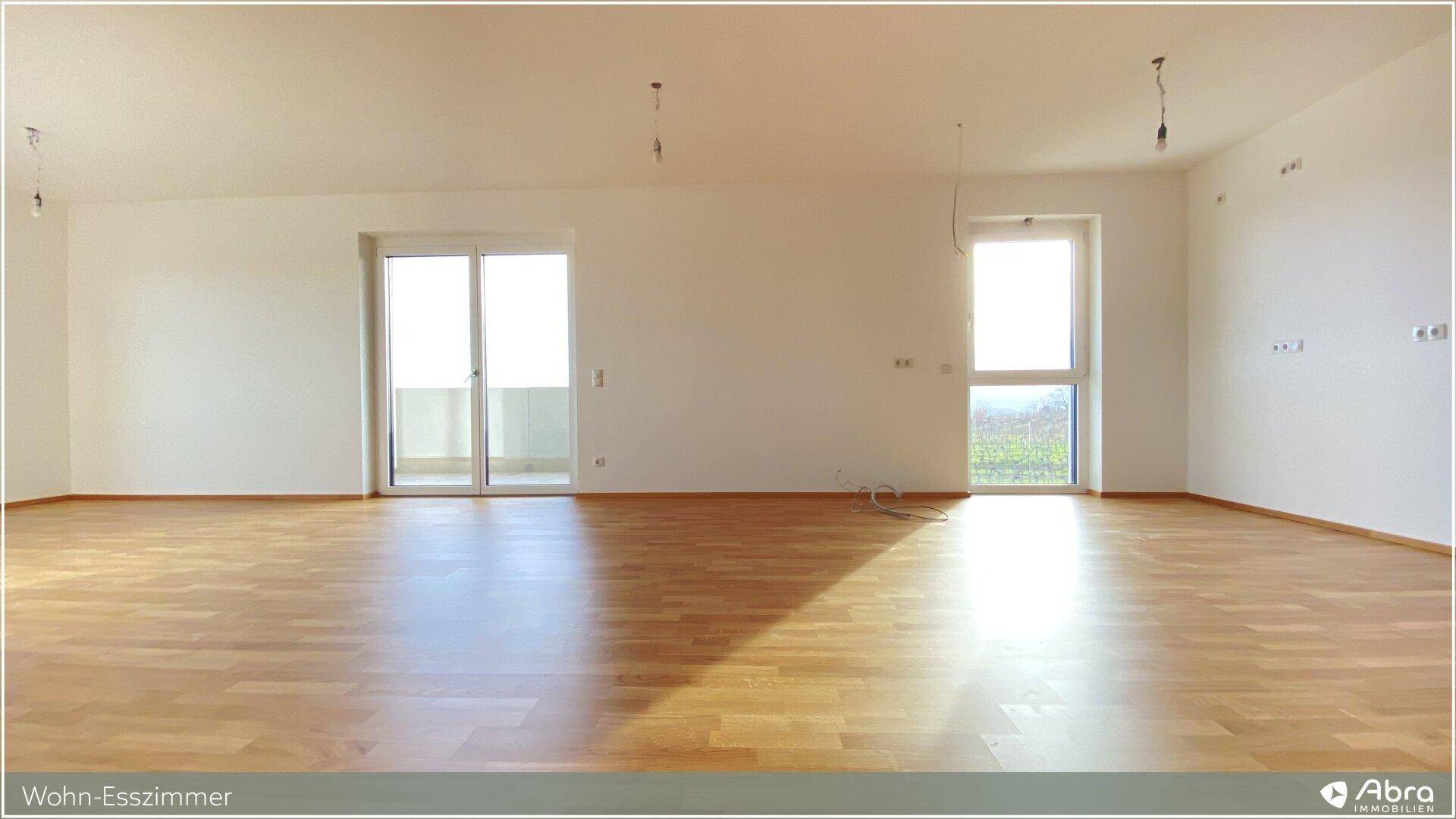 Lichtdurchfluteter Wohn-Essbereich mit Holzboden und großen Fenstern, die viel Tageslicht hereinlassen.