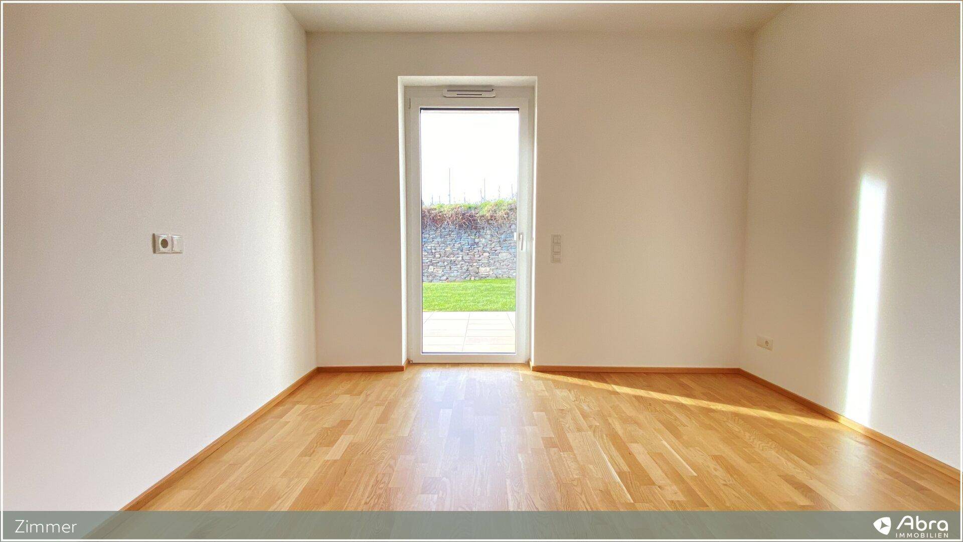 Geräumiges Zimmer mit Holzboden und viel Tageslicht durch die Terrassentür.