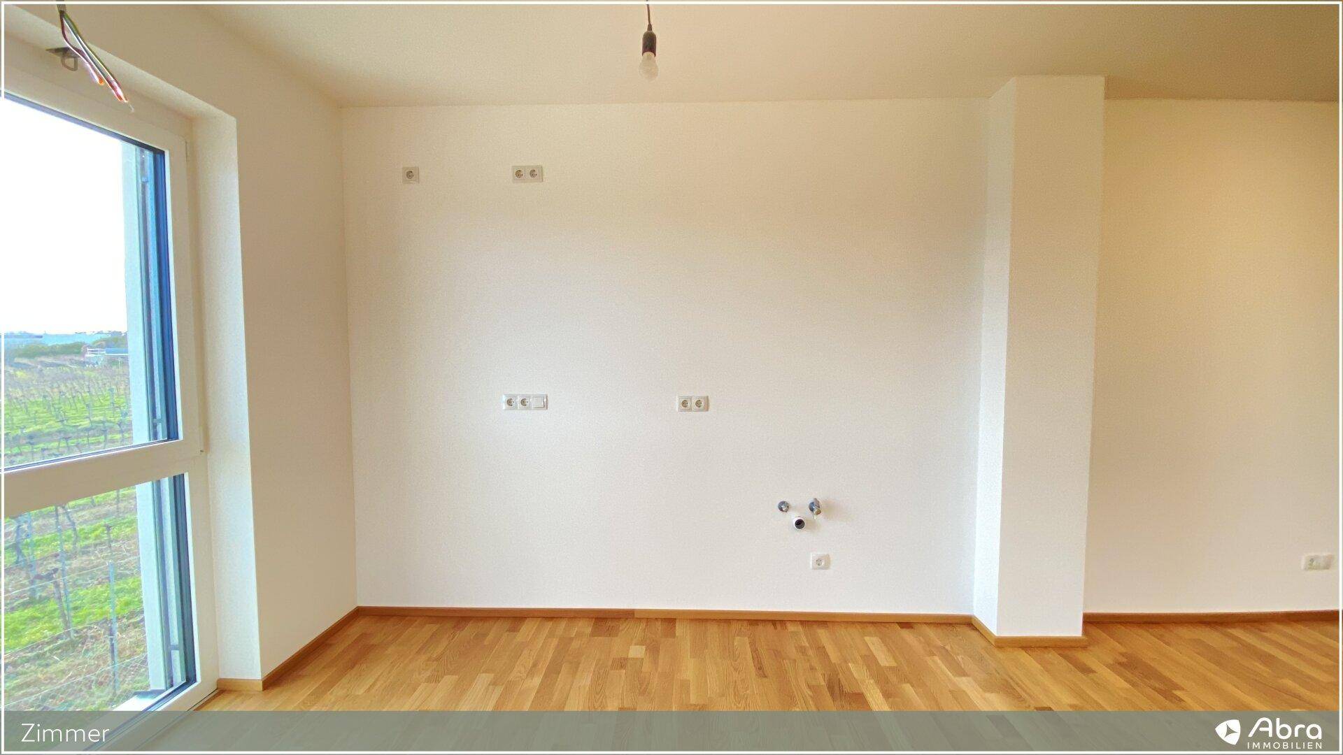 Helles Zimmer mit Parkettboden und großem Fenster, das einen Blick ins Grüne bietet.