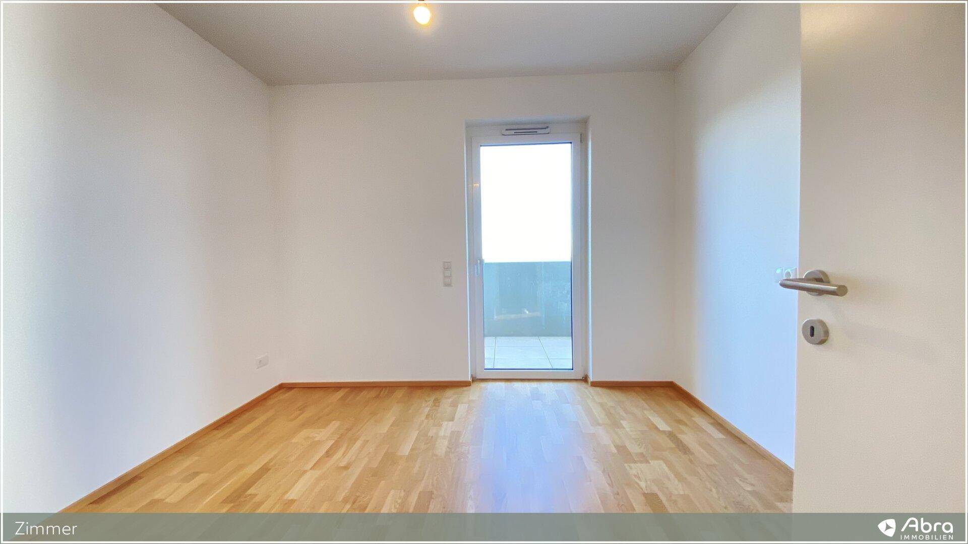 Helles Zimmer mit Holzboden und Balkonzugang, bietet viel natürliches Licht.