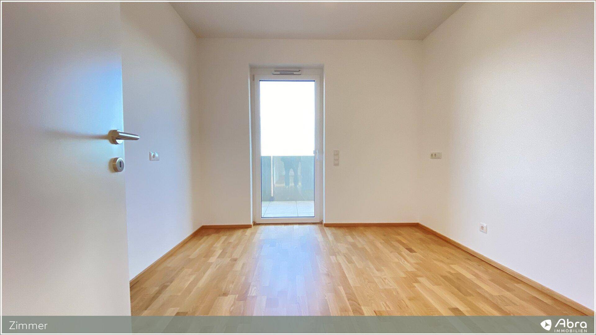 Freundliches Zimmer mit Parkettboden und Zugang zu einem Balkon, ideal für ein Schlafzimmer.
