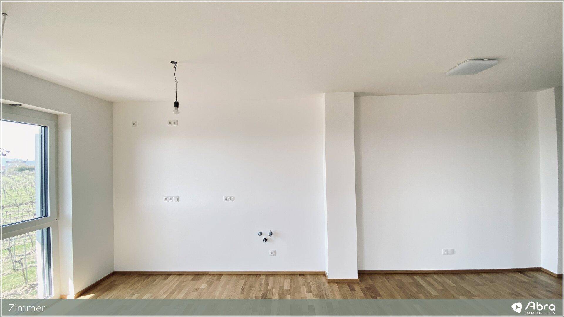 Geräumiges Zimmer mit Parkettboden und großem Fenster, das viel Licht hereinlässt.