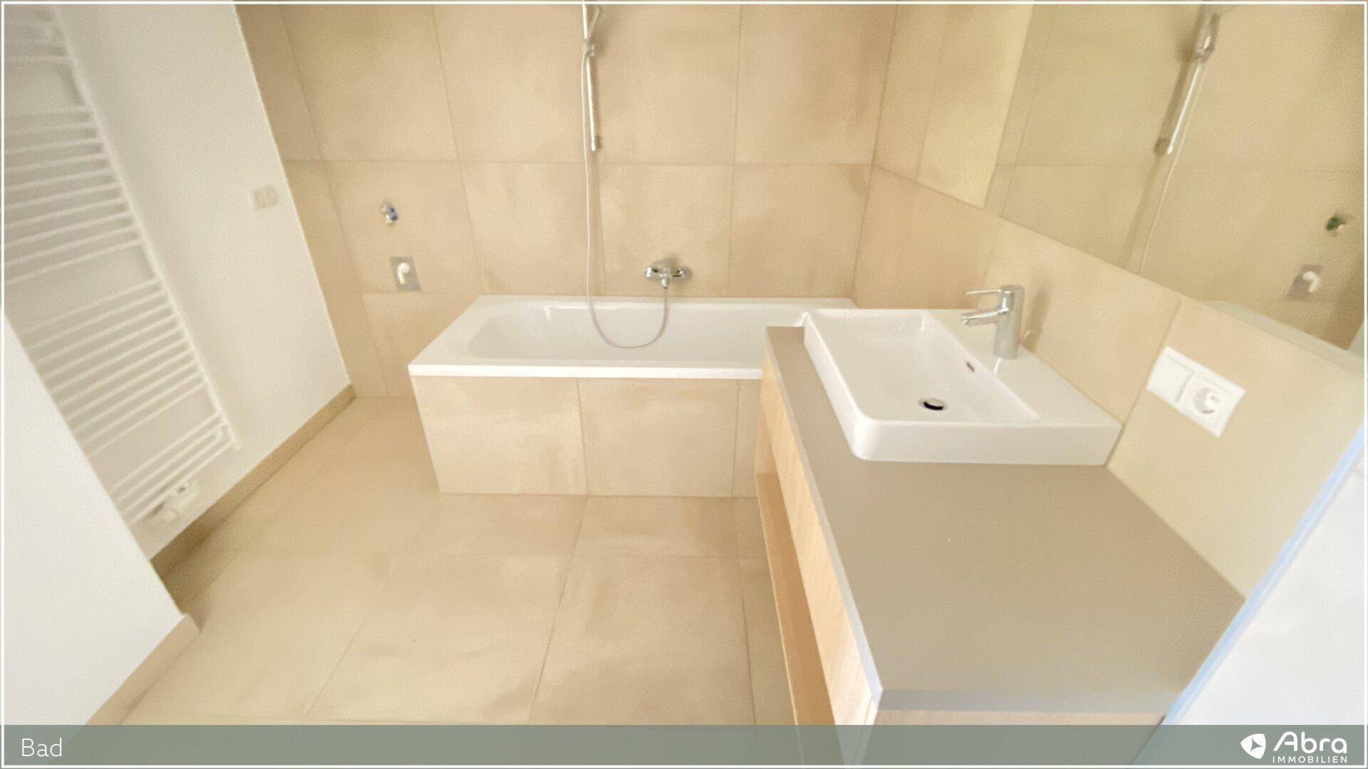 Modernes Badezimmer mit beigefarbenen Fliesen, Badewanne und Waschtisch.