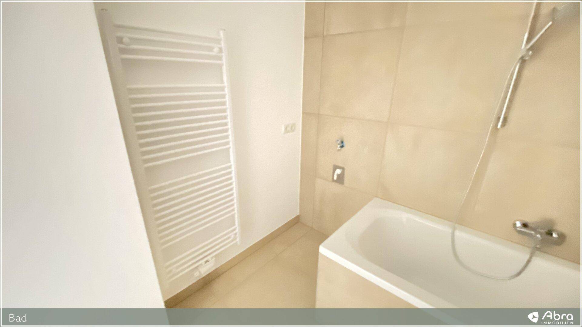 Badewanne und beheizter Handtuchhalter in einem modern gefliesten Badezimmer.