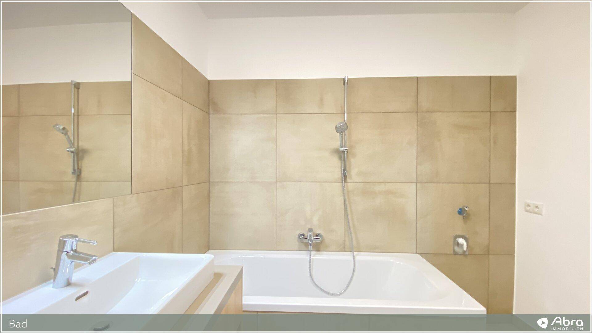 Badewanne mit Duschfunktion und Waschtisch in einem hell gefliesten Badezimmer.