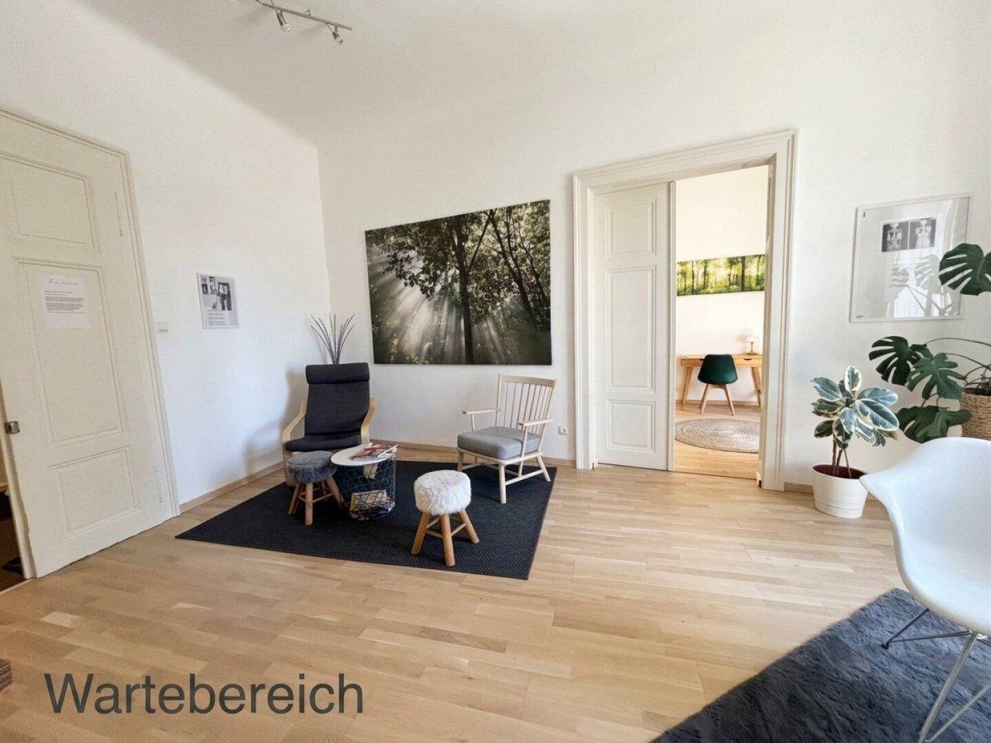 Heller Wartebereich mit Holzboden, bequemen Stühlen und einem Durchgang zu einem weiteren Raum.