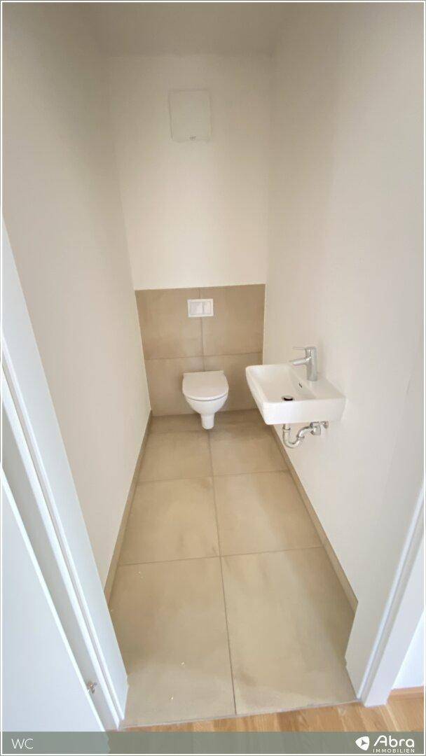 Separates Gäste-WC mit wandhängender Toilette und kleinem Handwaschbecken.