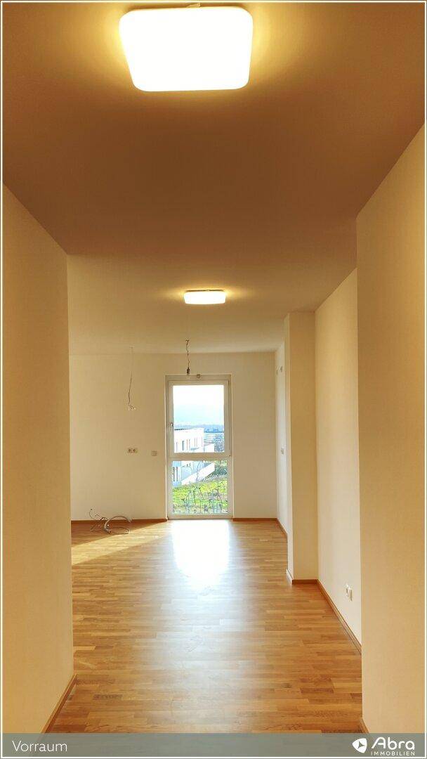 Lichtdurchfluteter Flur mit Holzparkettboden und Blick durch eine Fenstertür ins Grüne.