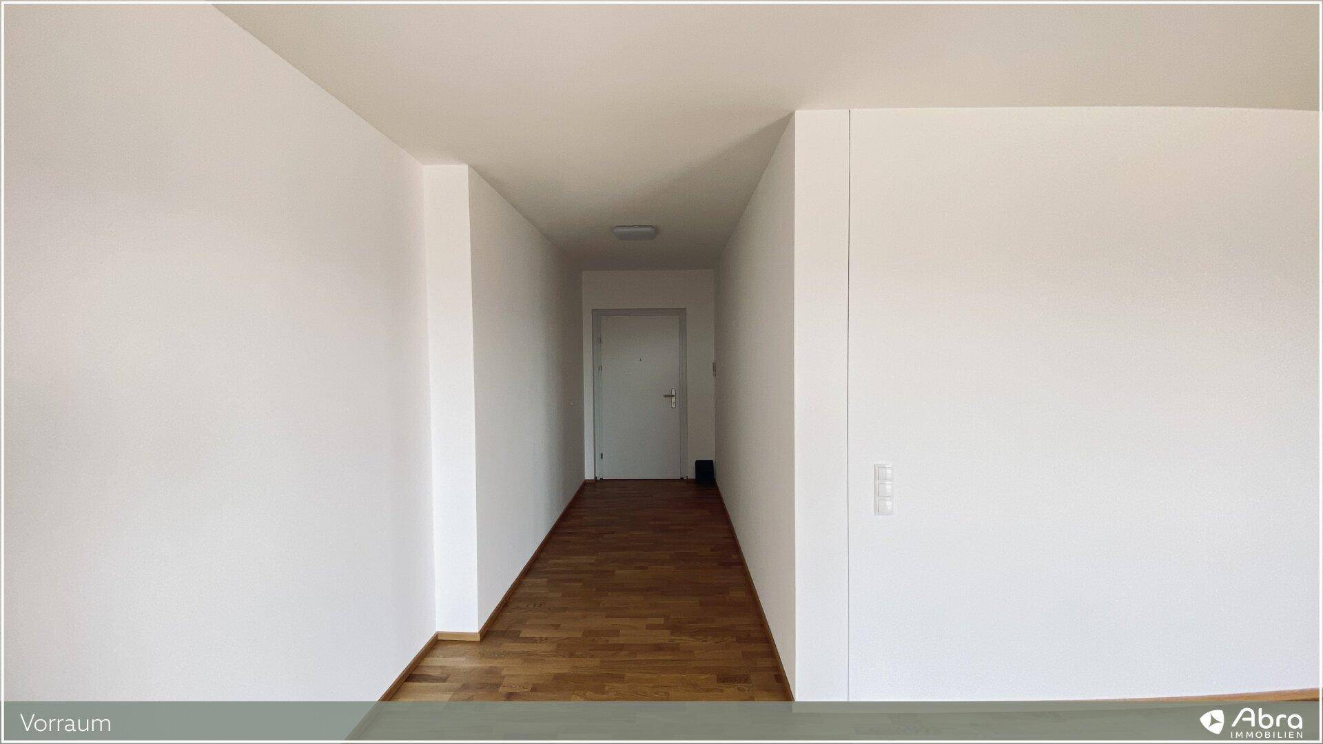Heller Wohnbereich mit Holzparkettboden und weiß gestrichenen Wänden, Blick zum Eingangsbereich.