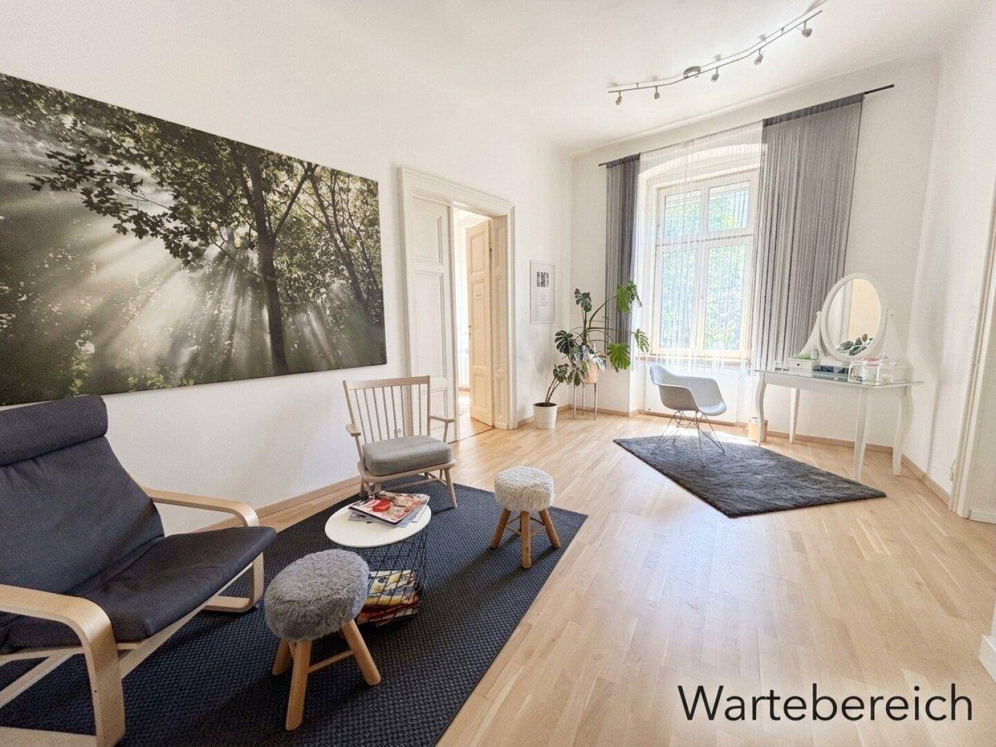 Geräumiger Wartebereich mit großem Fenster, Vorhängen, einem Schminktisch und hellem Holzboden.