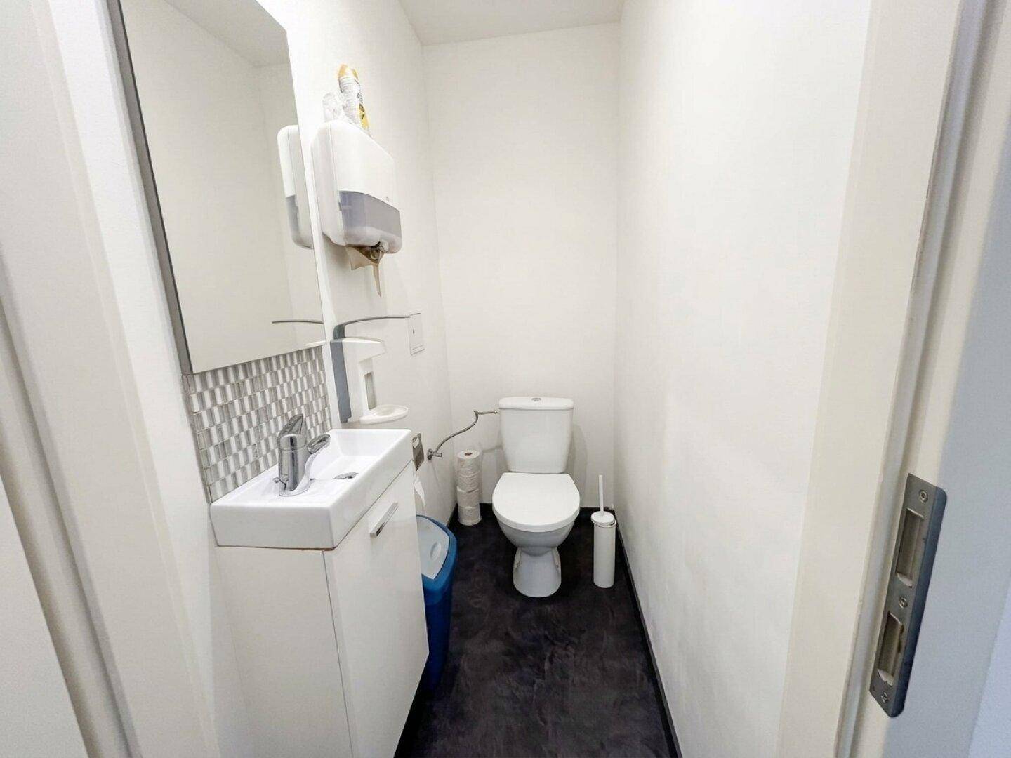 Kleines Gäste-WC mit Toilette, Waschbecken und einer modern gefliesten Rückwand.
