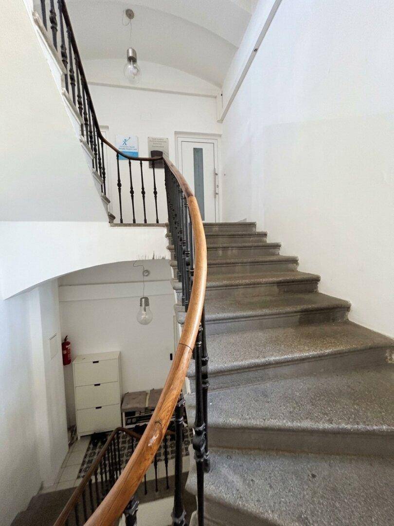 Historisches Treppenhaus mit Steinstufen, schmiedeeisernem Geländer und Holzhandlauf.