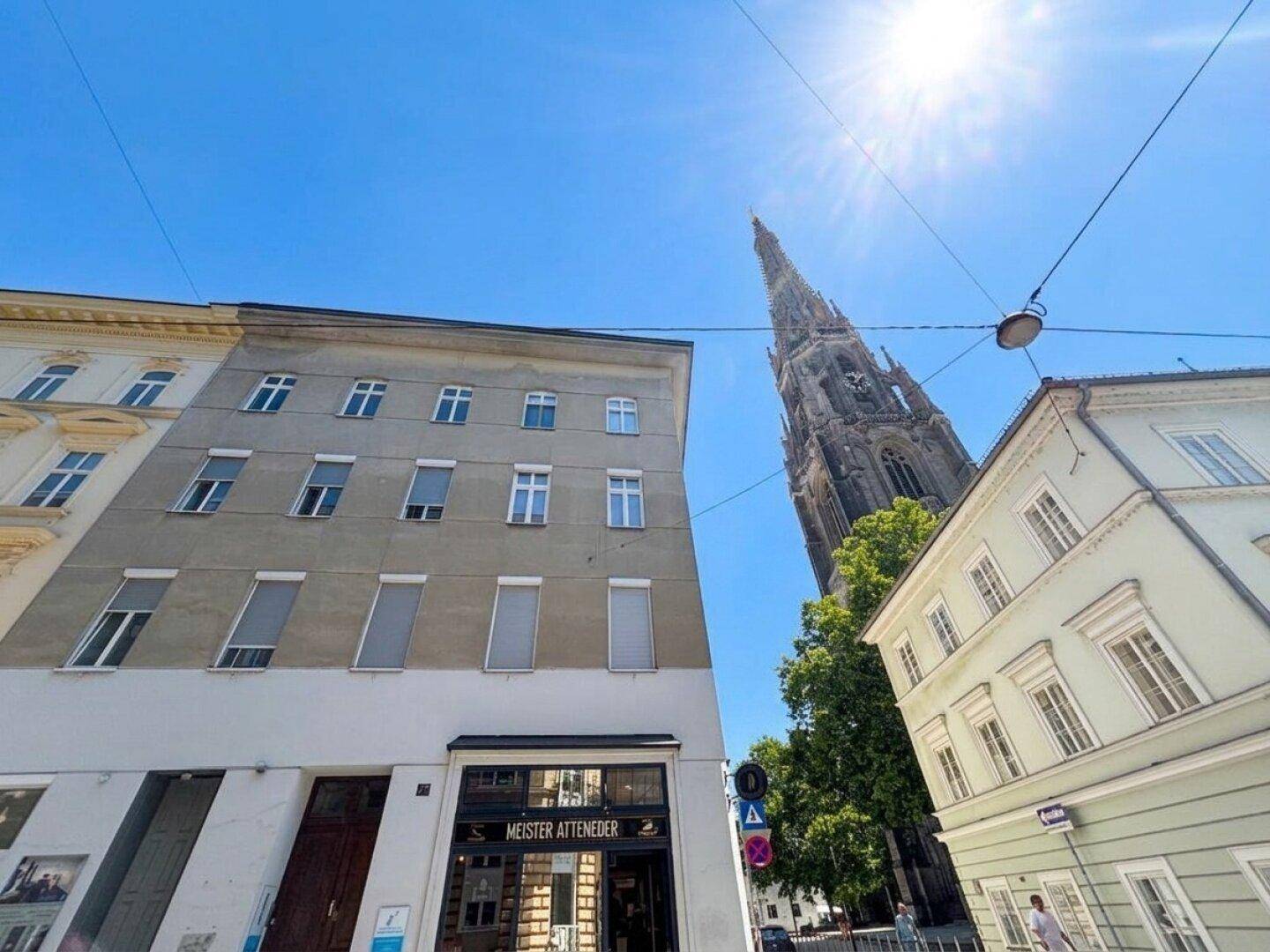 Straßenansicht mit mehreren Gebäuden und der Kirchturmspitze im Hintergrund unter blauem Himmel.