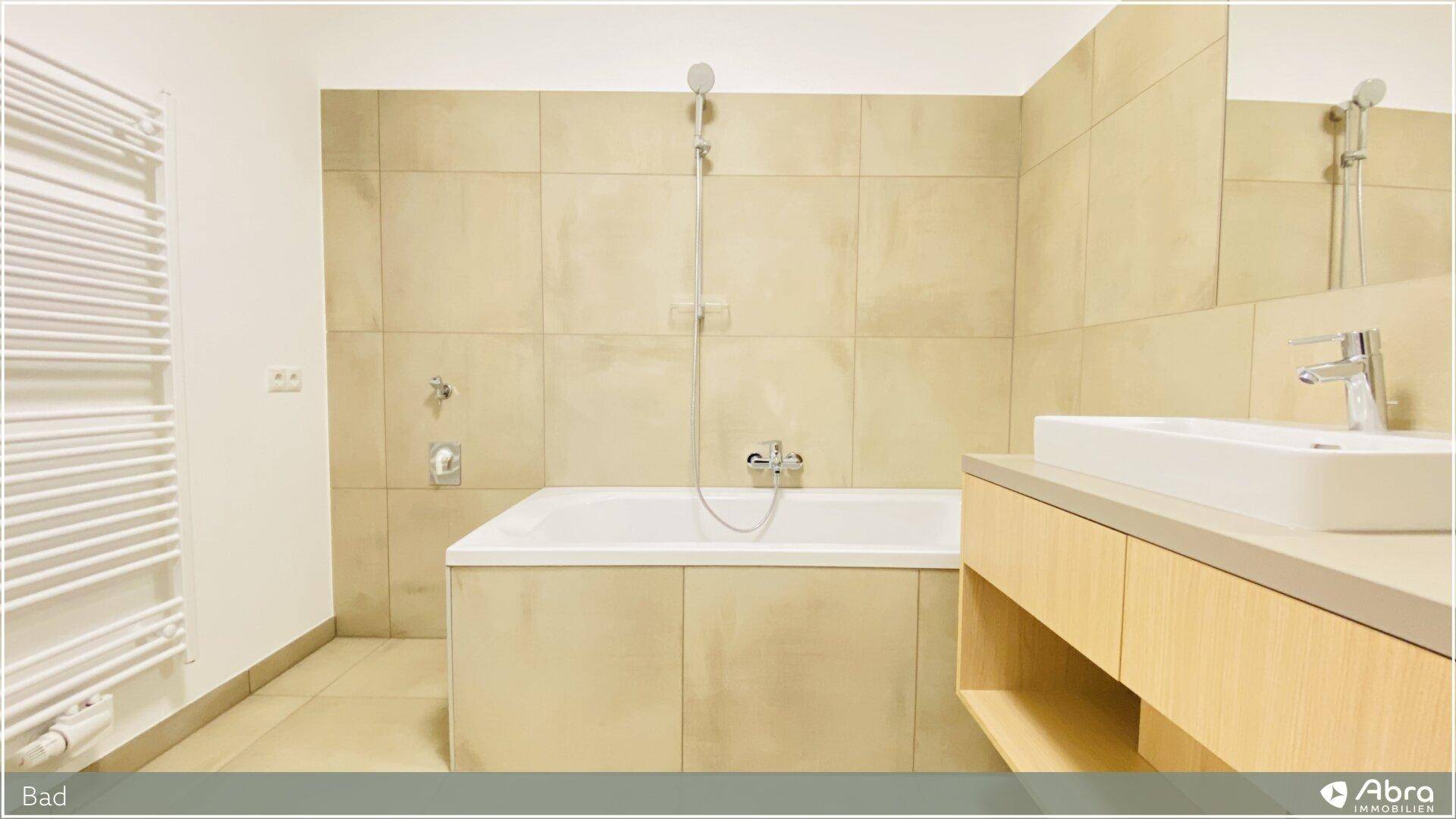 Modernes Badezimmer mit Badewanne, Waschtisch und beigefarbenen Fliesen.
