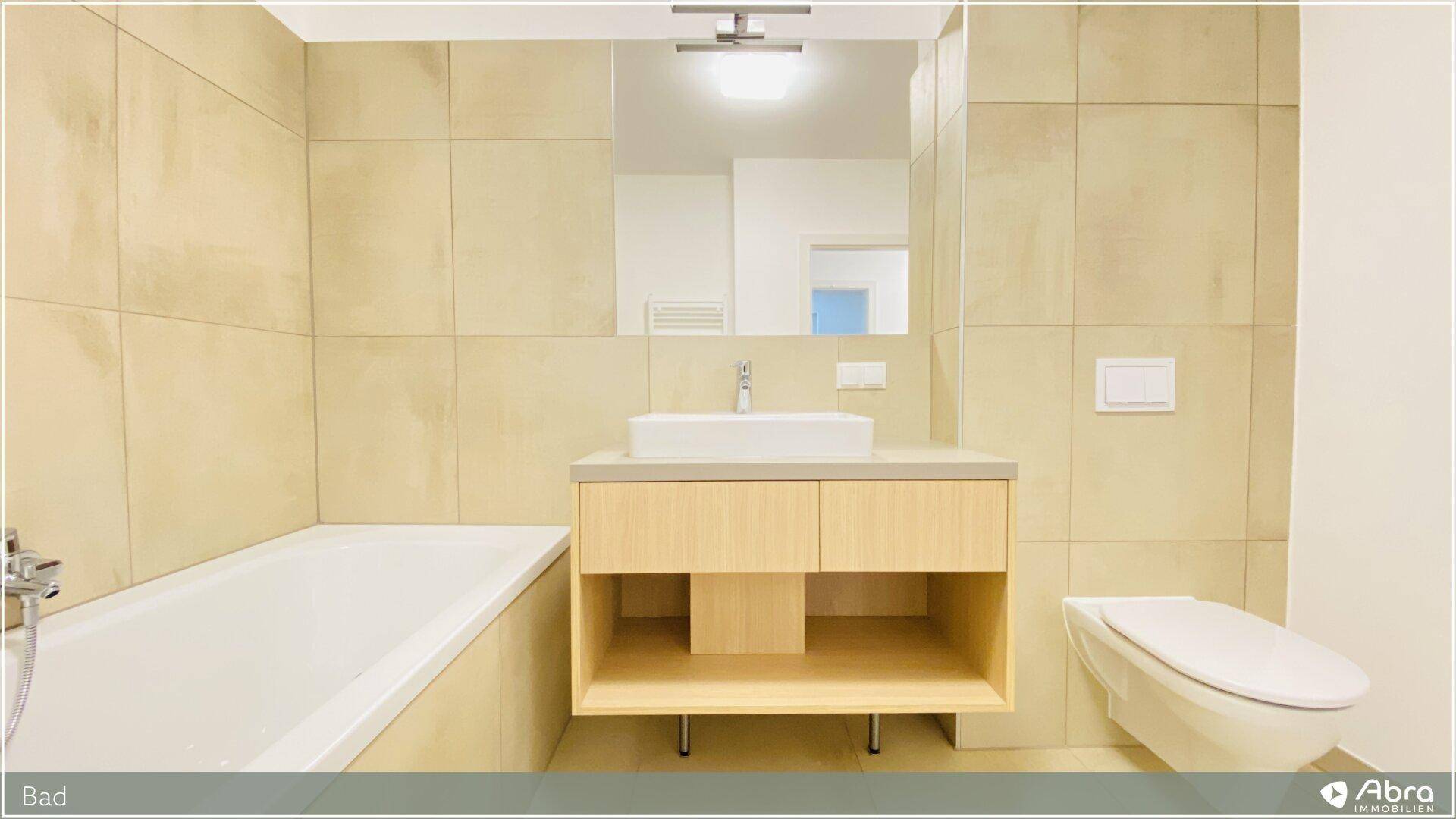 Helles Badezimmer mit Badewanne, modernem Waschtisch und wandhängendem WC.