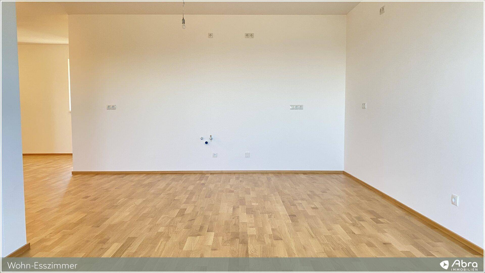 Heller, leerer Wohn-Essbereich mit Parkettboden und Anschlüssen für eine offene Küche.