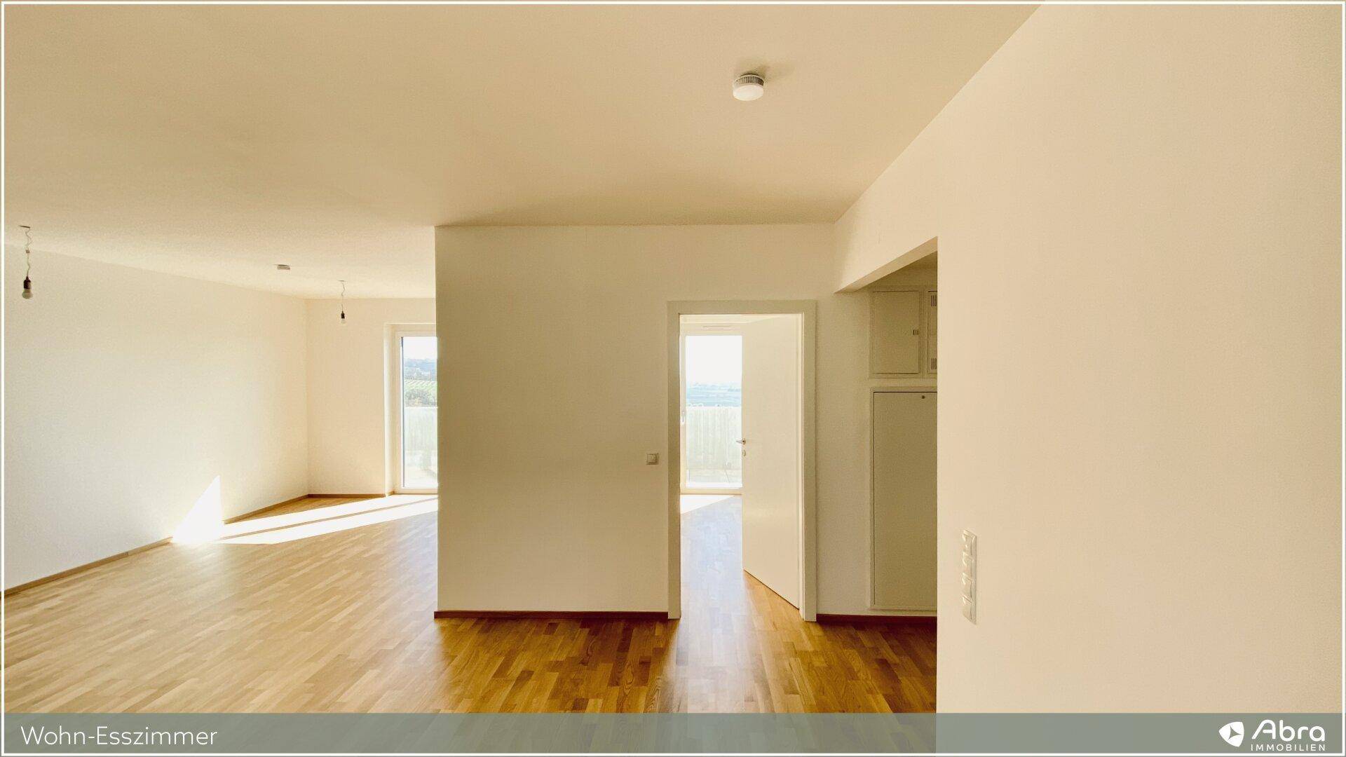Lichtdurchfluteter Wohn-Essbereich mit Holzboden und Zugang zu einem Balkon, ideal für offenes Wohnen.