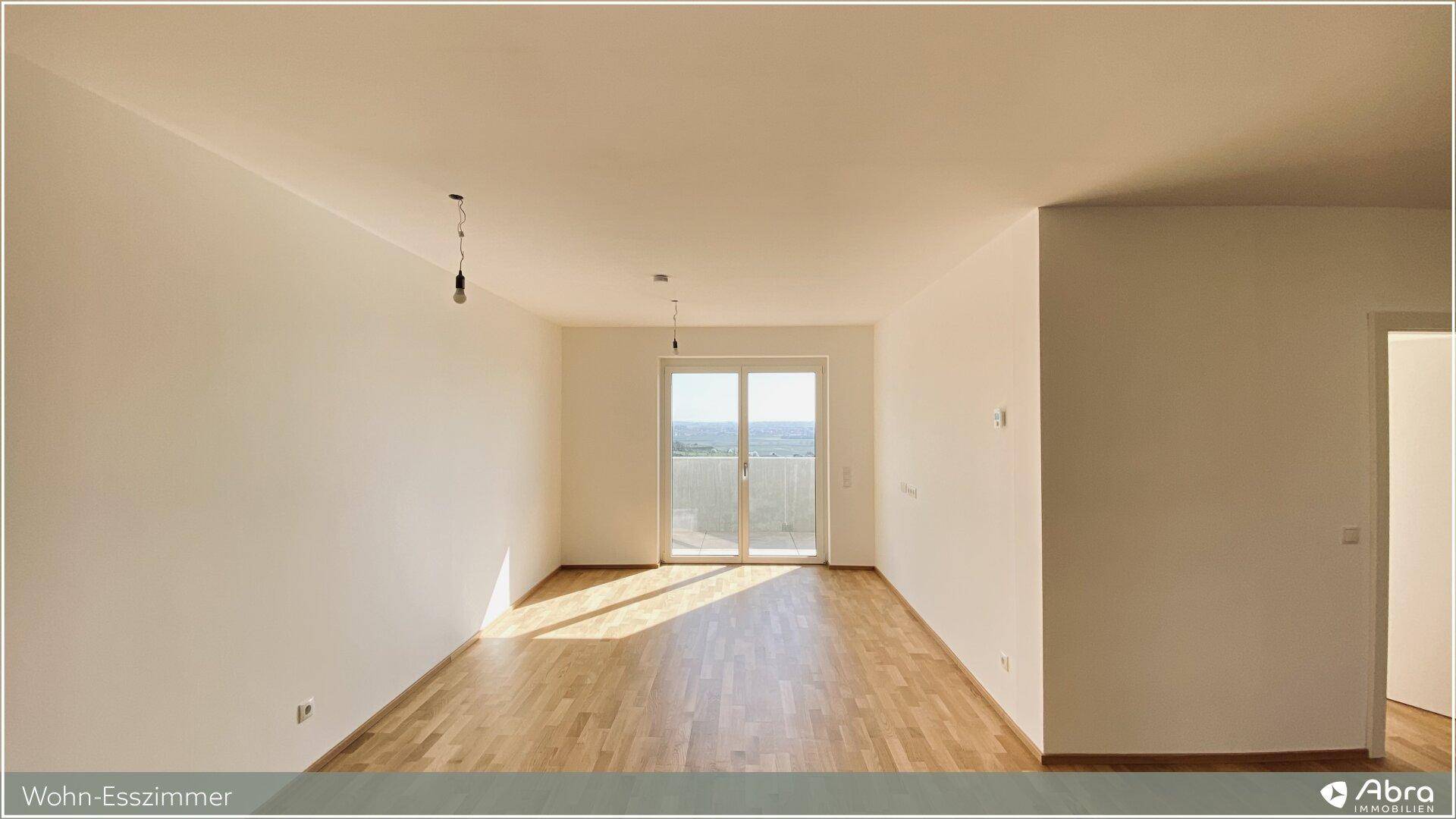 Heller Wohn-Essbereich mit Parkettboden und großer Balkontür, die viel Tageslicht hereinlässt.
