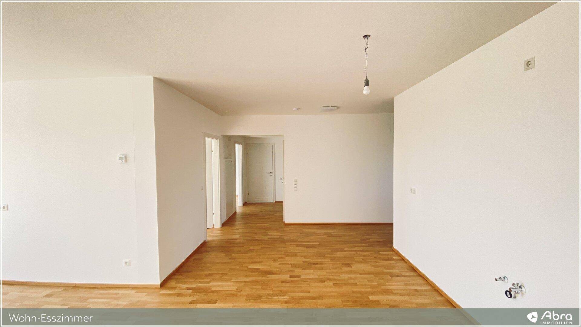 Offener Wohn-Essbereich mit Holzboden und Durchgang zu weiteren Zimmern und dem Flur.