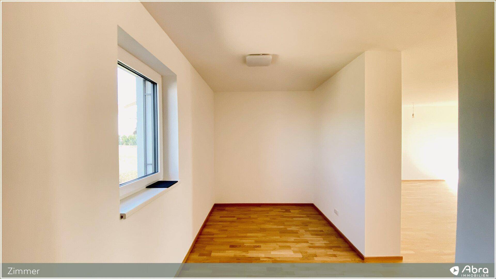 Unmöbliertes Zimmer mit Parkettboden und Fenster, das viel Tageslicht hereinlässt.