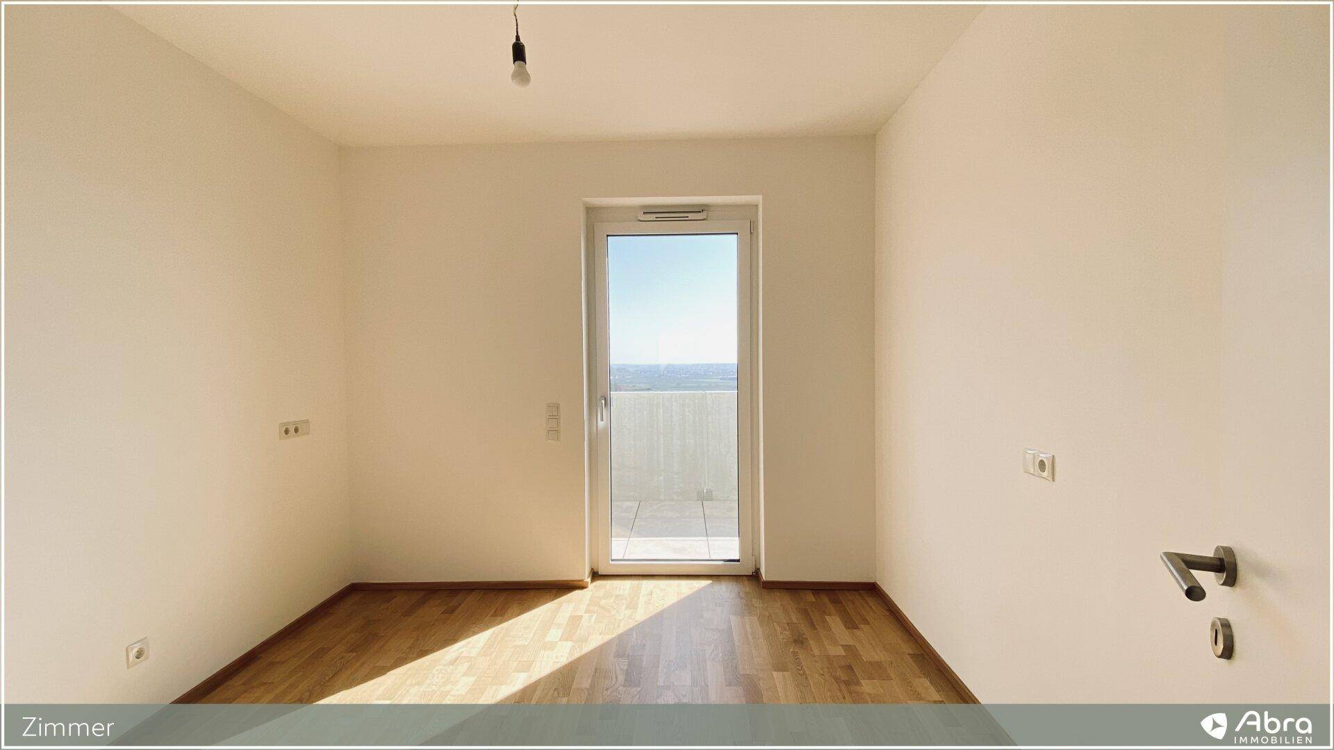 Helles Zimmer mit Parkettboden und Balkontür, die Zugang zum Außenbereich bietet.
