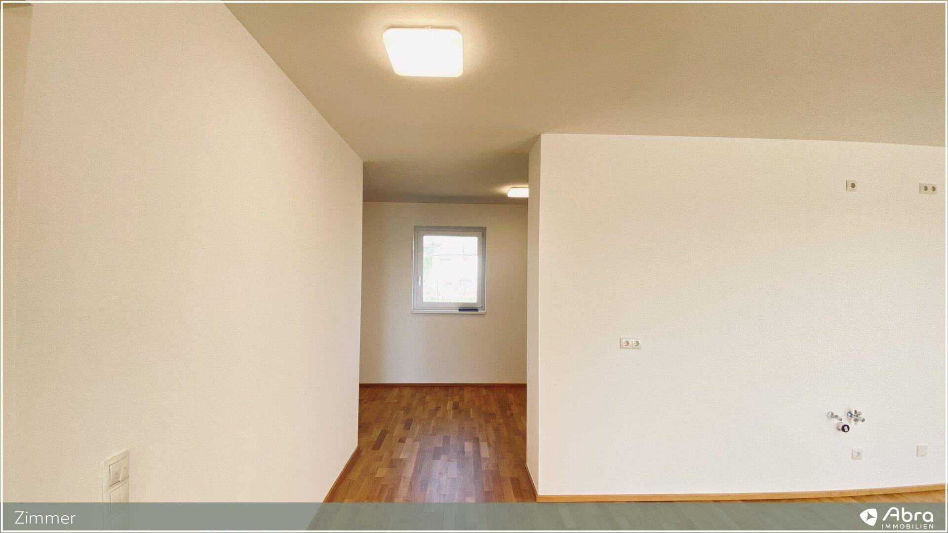Heller Flur mit Parkettboden und Fenster, der zu weiteren Räumen der Wohnung führt.