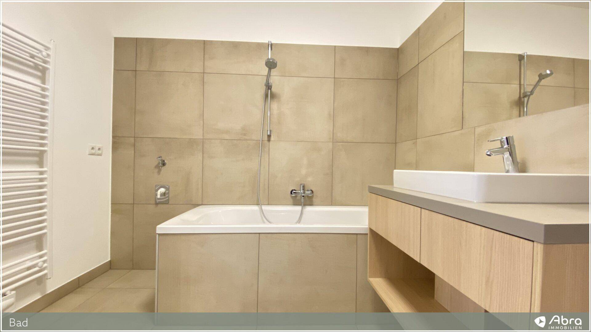 Modernes Badezimmer mit Badewanne, Waschtisch und beigefarbenen Fliesen, inklusive Handtuchheizkörper.