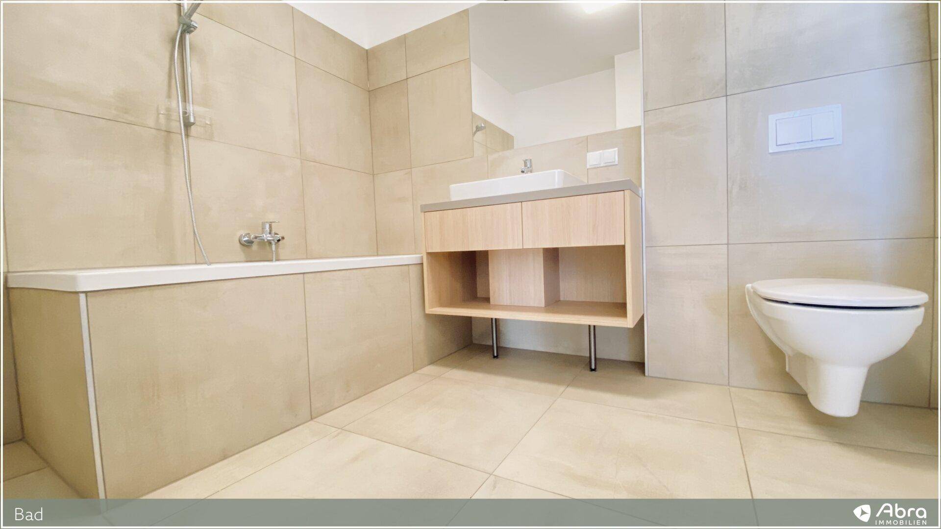 Zeitgemäßes Badezimmer mit Waschtisch, wandhängender Toilette und Badewanne, gefliest in Beige.